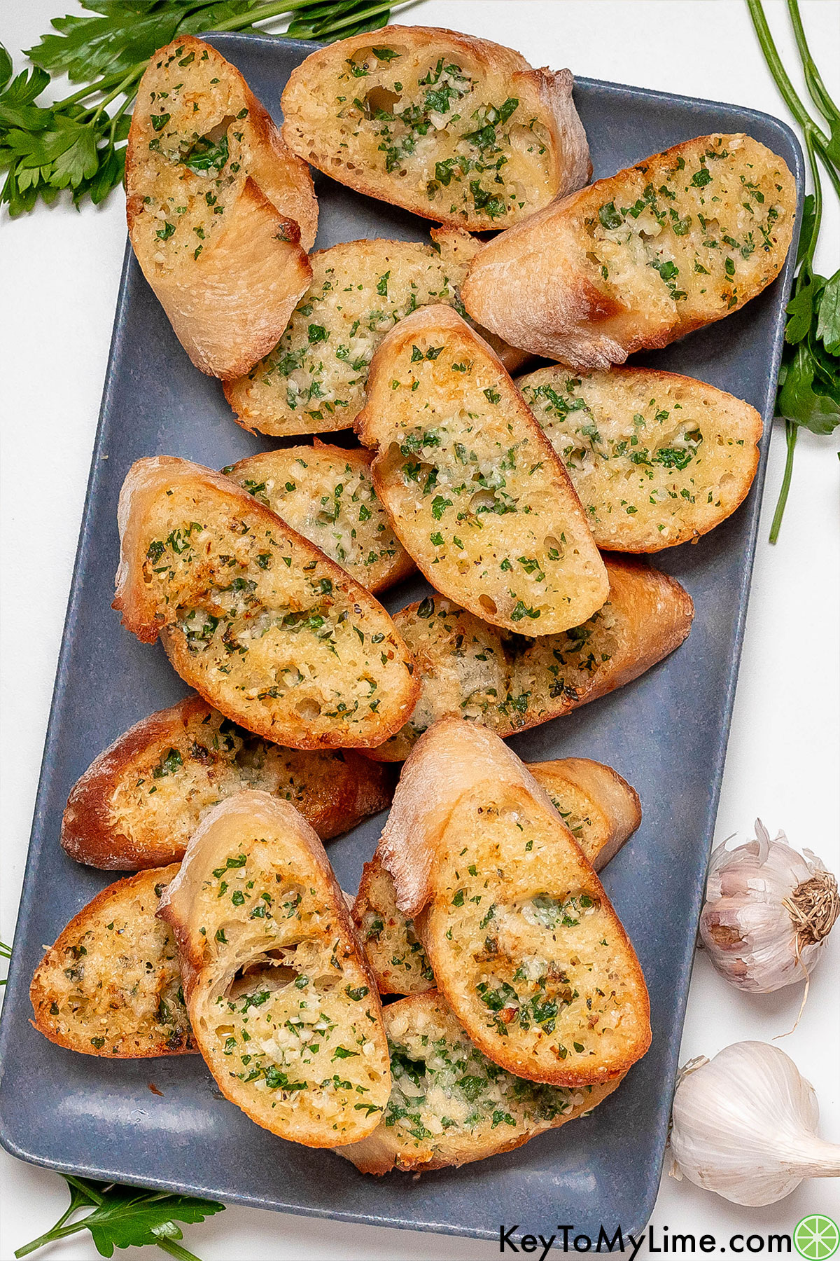 An overhead image of cooked garlic bread with fresh garlic and parsley to the side.
