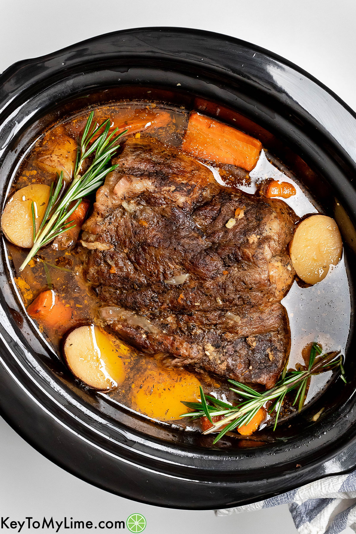 An overhead image of a fully cooked pork roast resting in slow cooker with potatoes and carrots throughout.