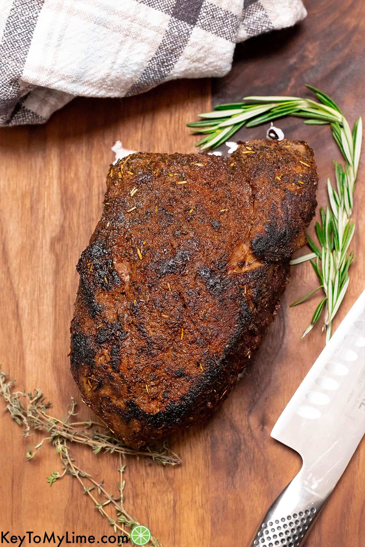 An overhead image of a fully cooked whole roast resting on a cutting board with fresh herbs to the side.