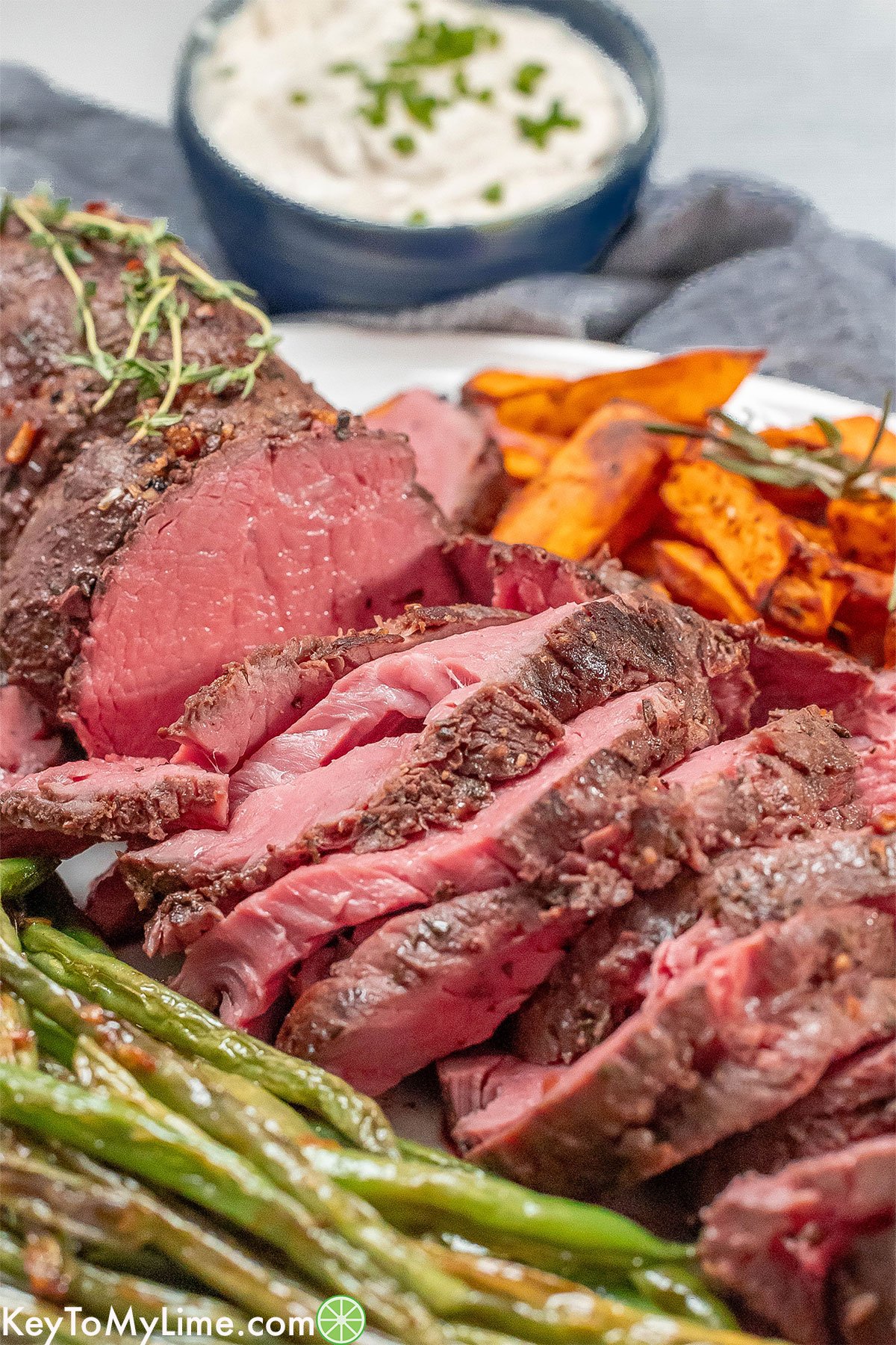 A side image of a partially sliced beef tenderloin next to a serving of green beans and sweet potatoes.