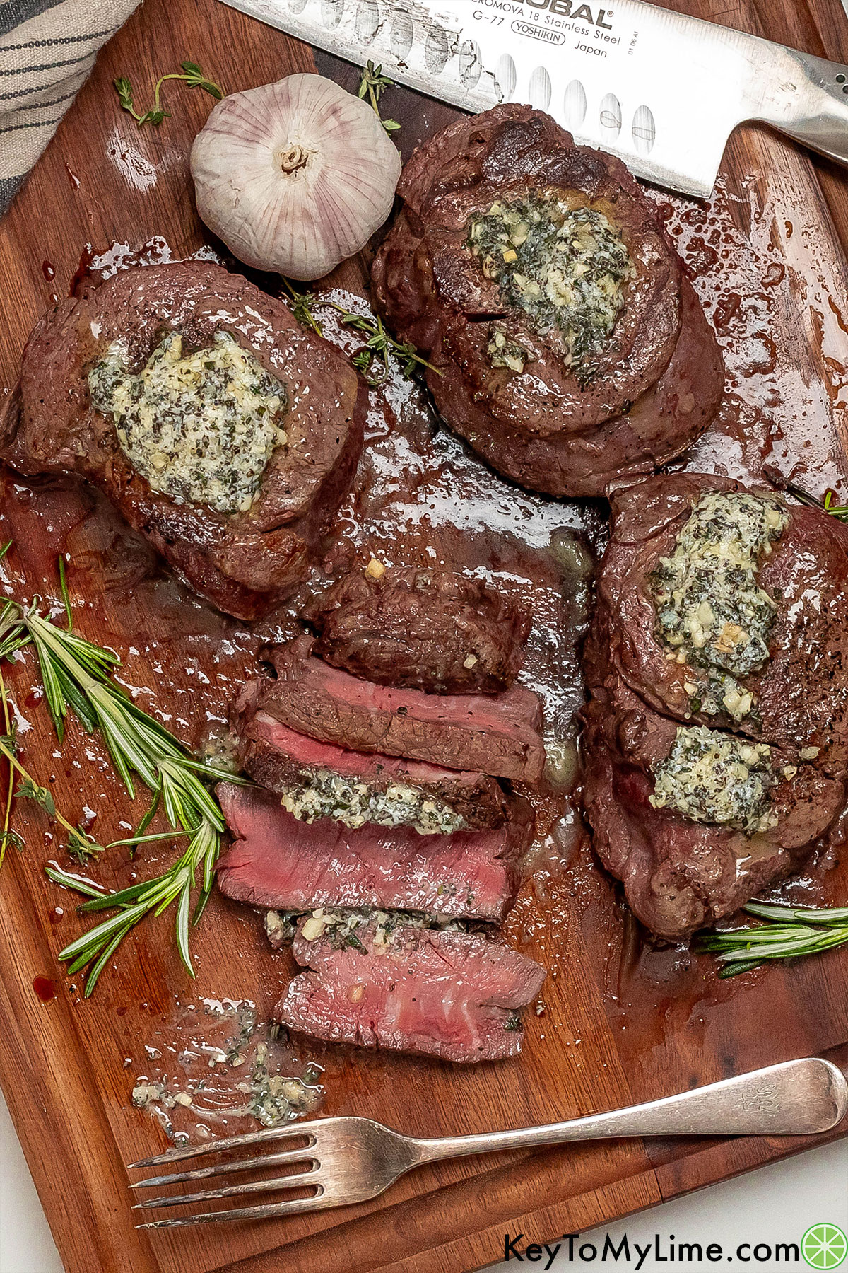 Whole and sliced filet mignon topped with garlic butter on a dark wood cutting board.