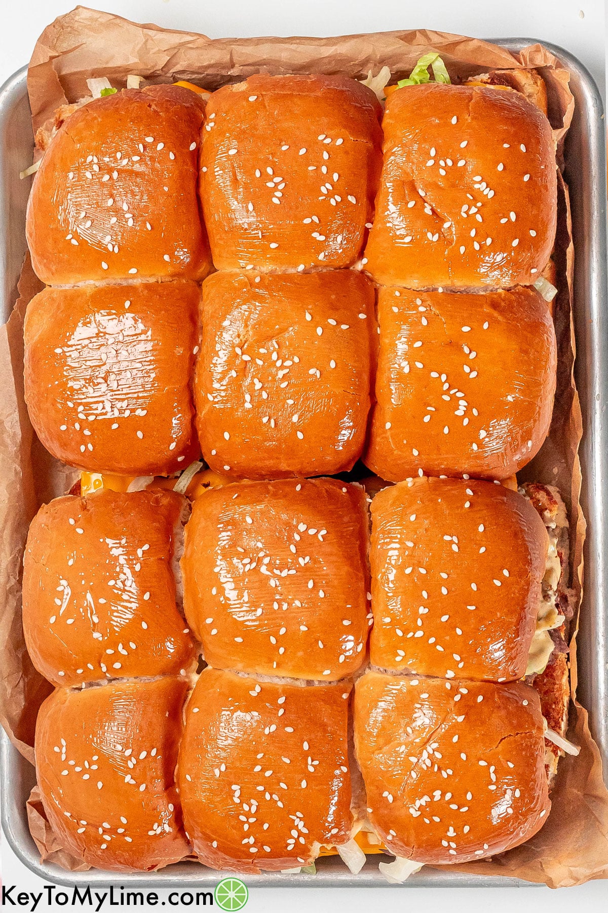 An overhead image of a sheet filled with sliders covered in butter on top of the buns.