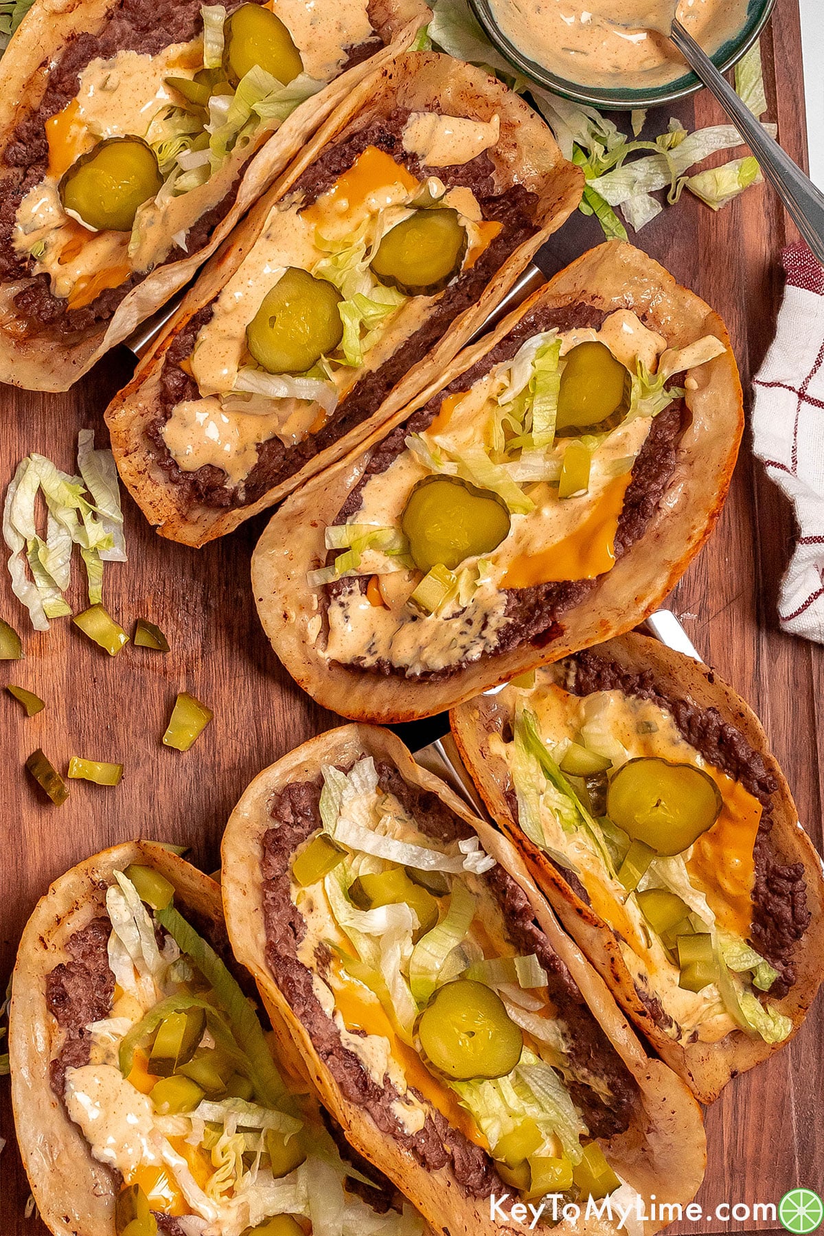 An overhead image of two rows of tacos filled with lettuce, pickles, and sauce throughout.