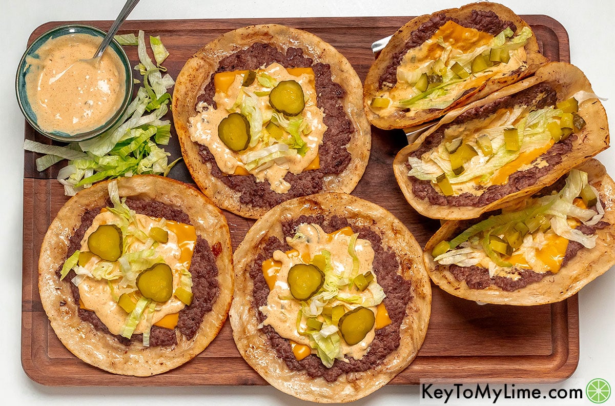 Adding lettuce, pickles, and big mac sauce on the tacos before serving.