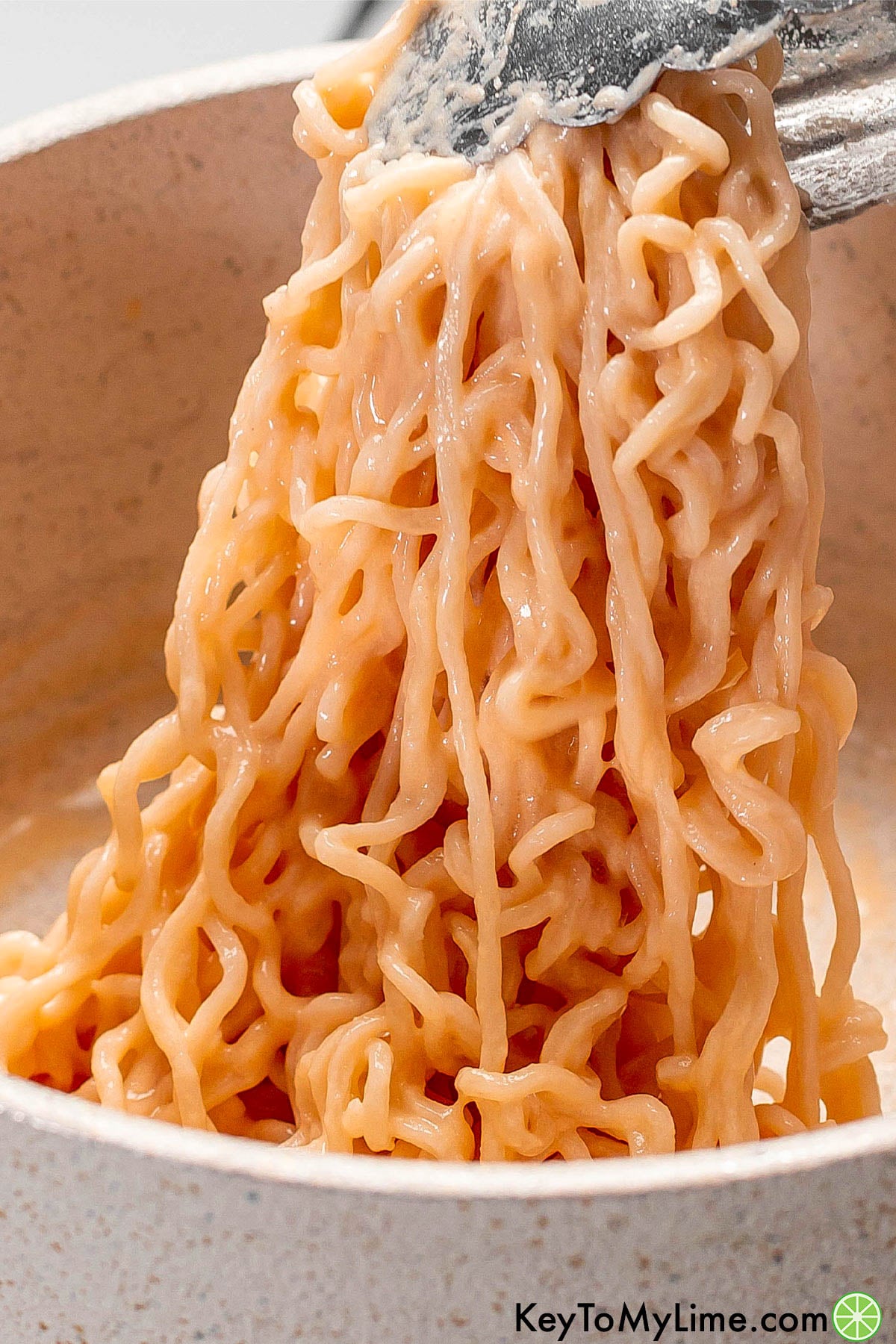 A close up image of tongs lifting up the cheesy ramen.