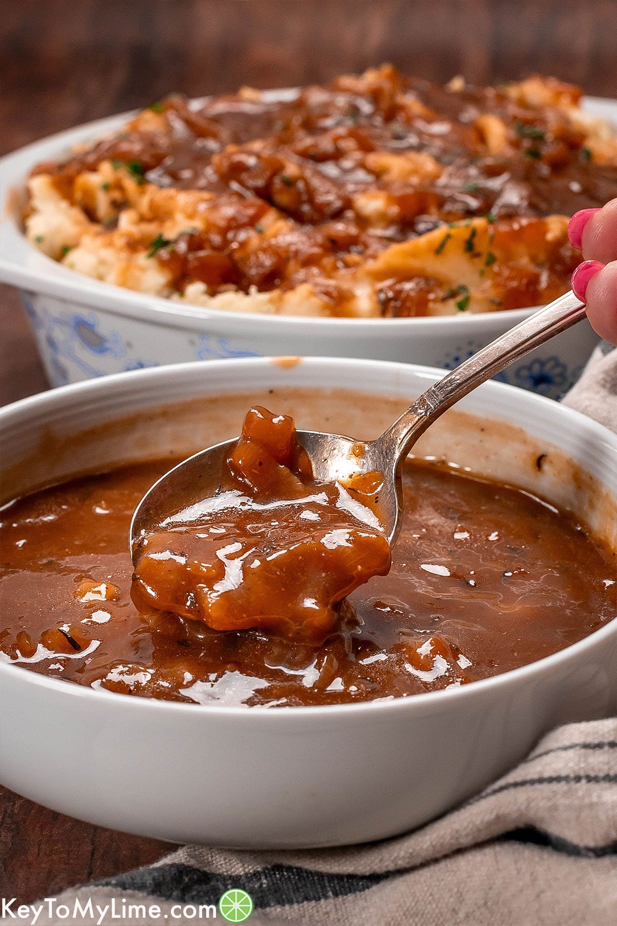 A side image of a bowl of gravy with a spoon lifting up showing the texture of the onion gravy.
