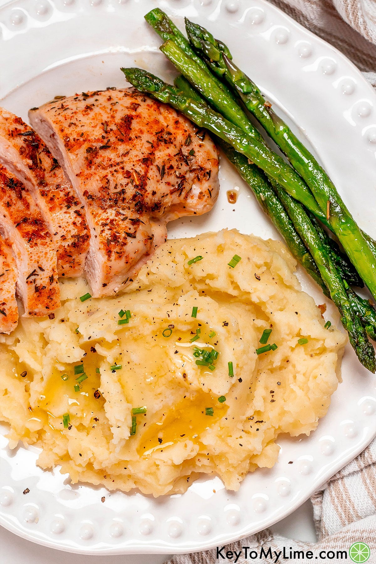 A plate filled with mashed potatoes with a side of asparagus and tenderloin.