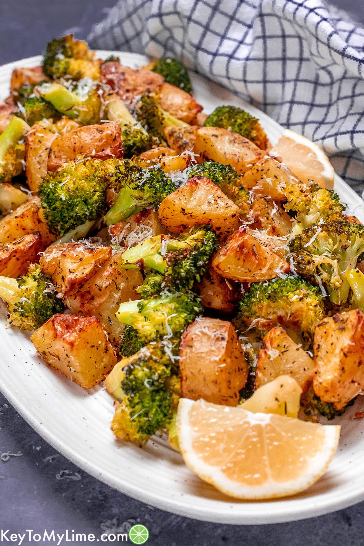 A side image of golden brown roasted potatoes and broccoli with lemon wedges on a large white platter.