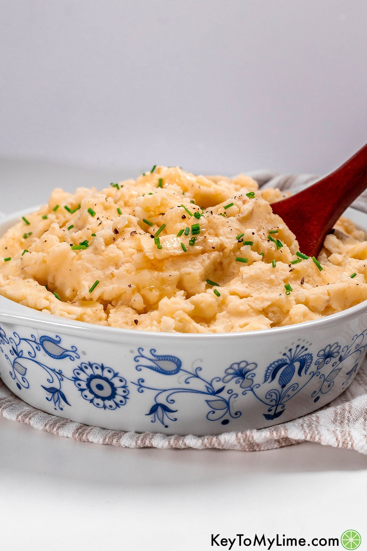 A side image of mashed potatoes in a beautiful serving dish with with a serving spoon resting inside.