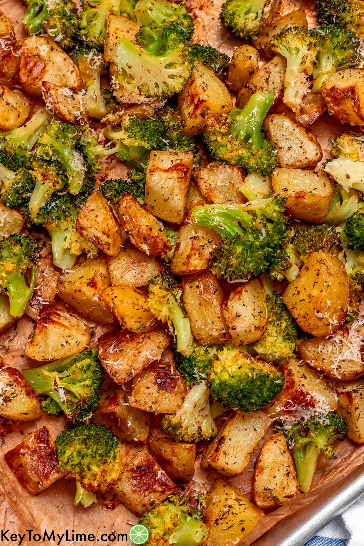 A close up image of fully roasted broccoli and potatoes on a baking sheet.