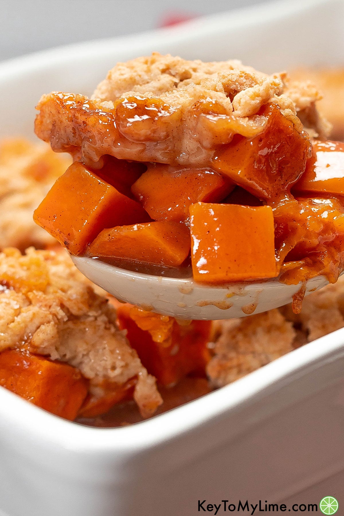 A side image of a serving spoon lifting up a scoop of sweet potato cobbler.