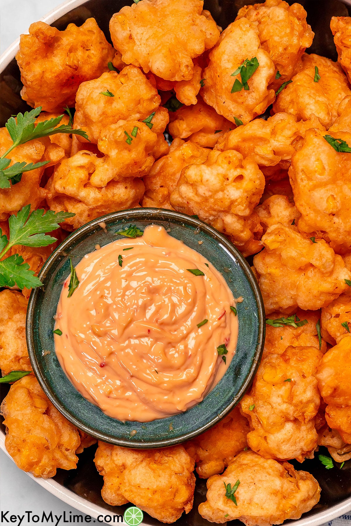 An overhead image of corn nuggets served on a large platter with garnish to the side.