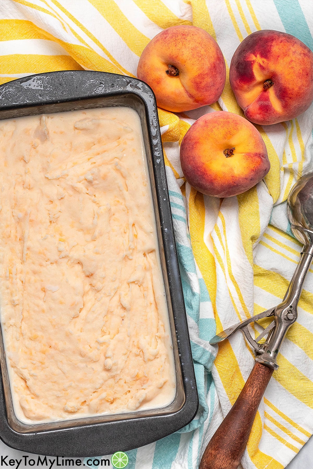 Overhead image of ice cream resting in a pan with peaches to the side.