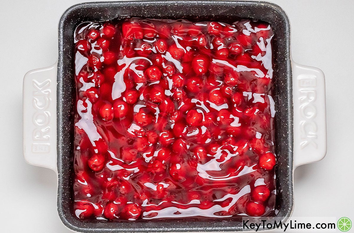 Adding cherry pie filling to the baking dish, and then mixing in vanilla evenly throughout.