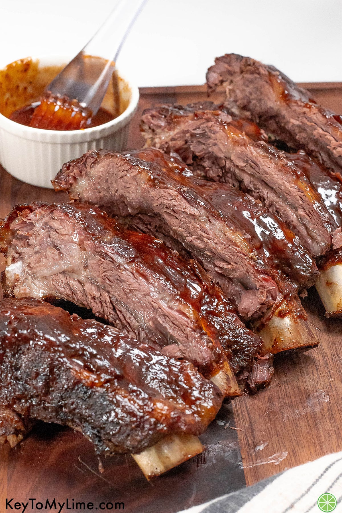 Sliced beef ribs on a cutting board with BBQ sauce in the background.