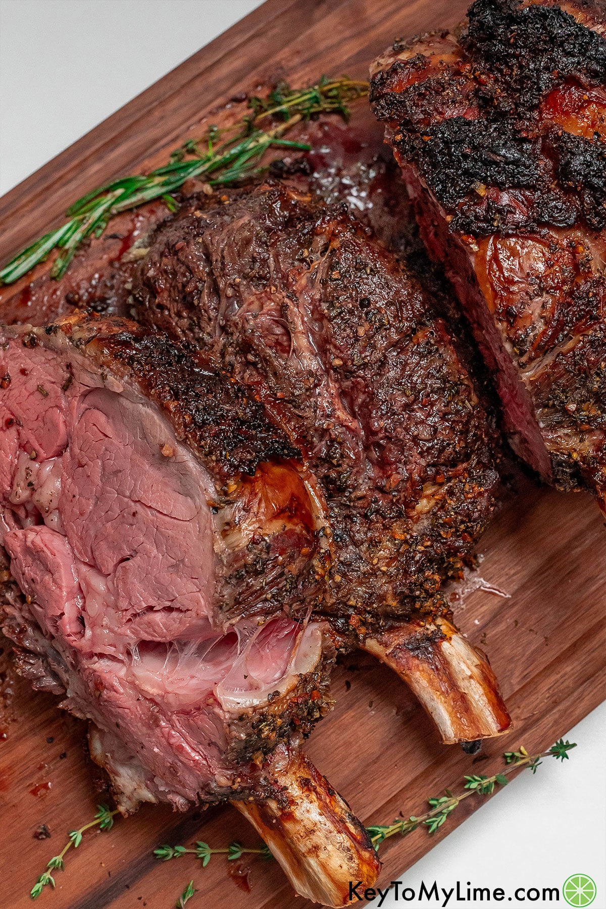 A beautifully crusted bone-in ribeye roast next to rosemary sprig.