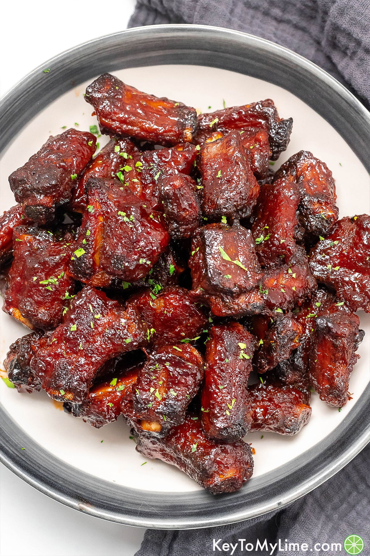 Freshly baked pork riblets served on a large plate with fresh parsley on top.