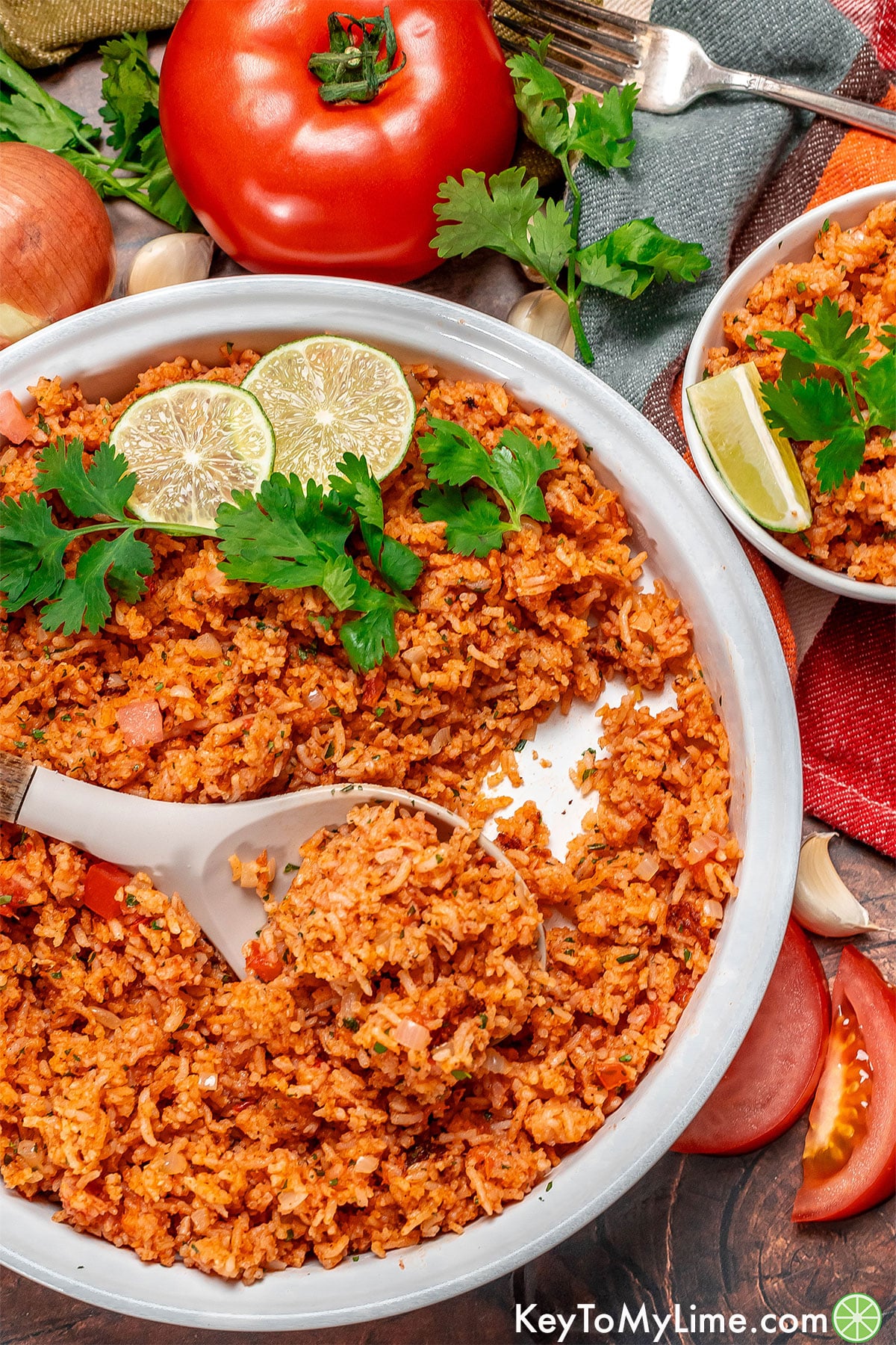 An overhead image of a partially filled serving dish filled with Mexican rice and vegetables to the side.