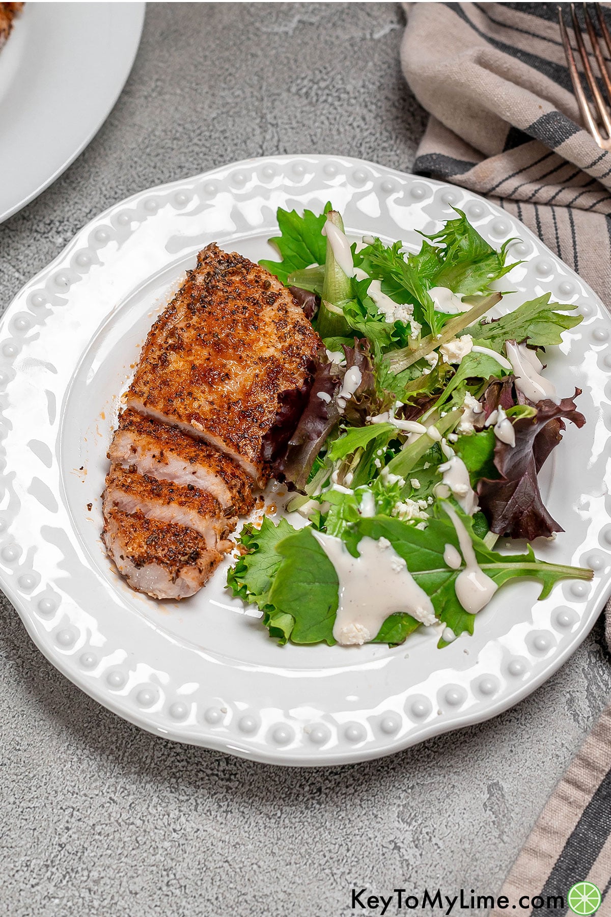 A boneless pork chop cut into slices with a green salad to the side.