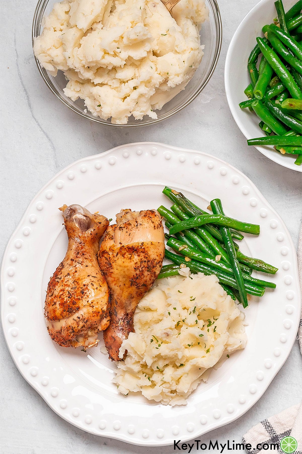 An overhead image of a serving of a chicken dinner with a couple of cooked vegetables to the side.