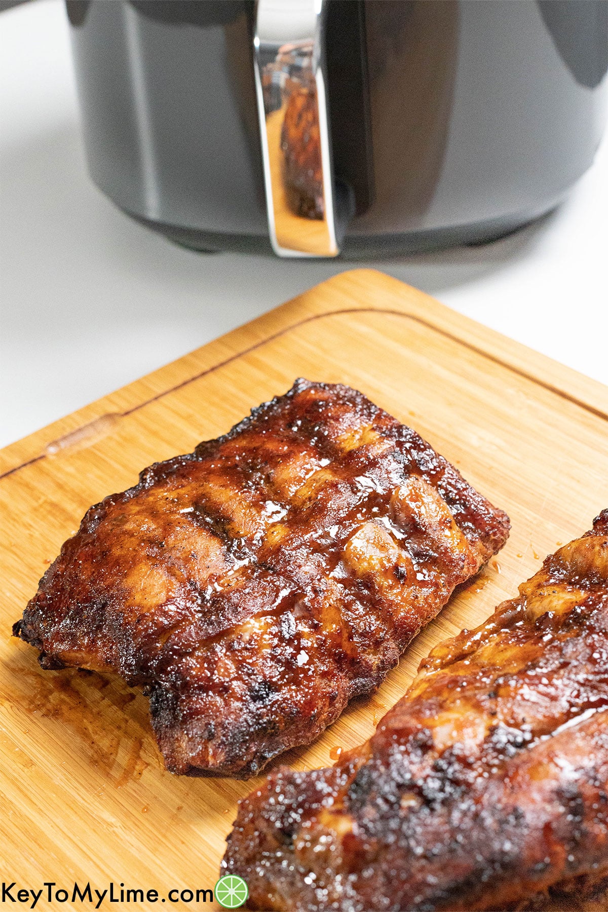 A set of two ribs on a cutting board with air fryer in the background.