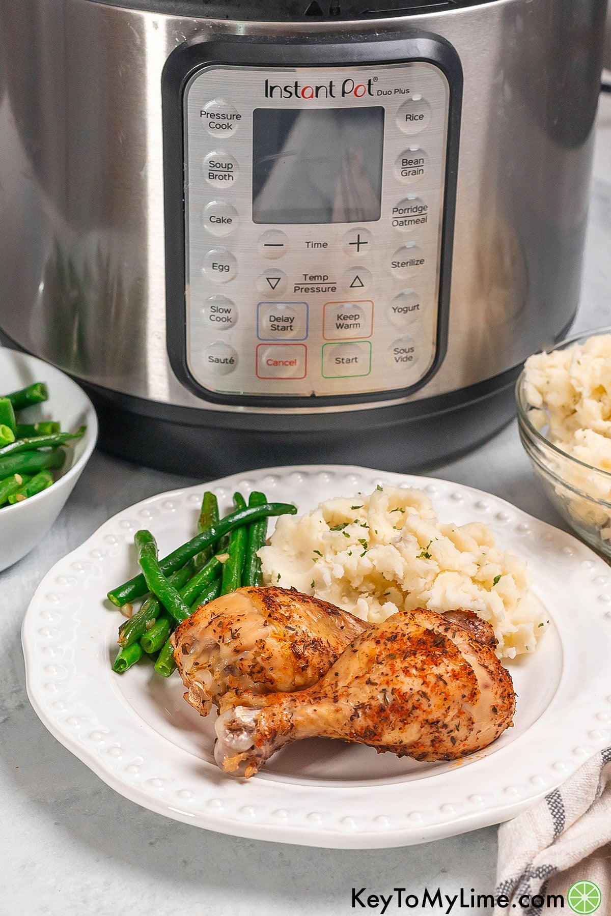 A side image of crispy chicken drumsticks with a serving of green beans on a white plate.