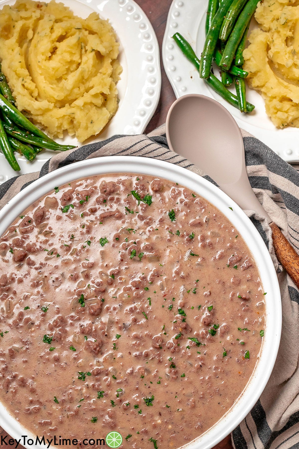 An overhead image of a serving dish filled with freshly made hamburger gravy next to a serving spoon.