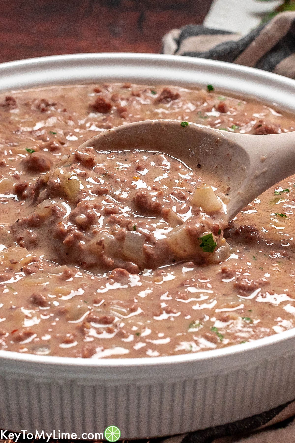 A close up of a serving spoon lifting up hamburger gravy out of a serving dish.