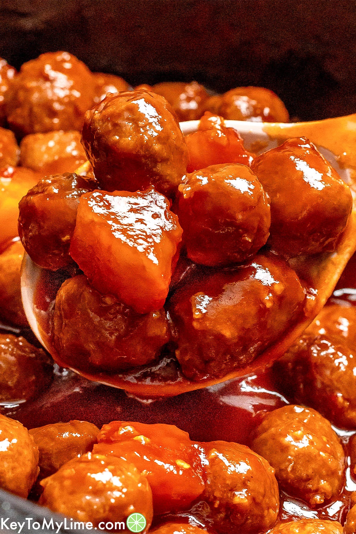 A close up meatballs on a serving spoon covered in sauce.