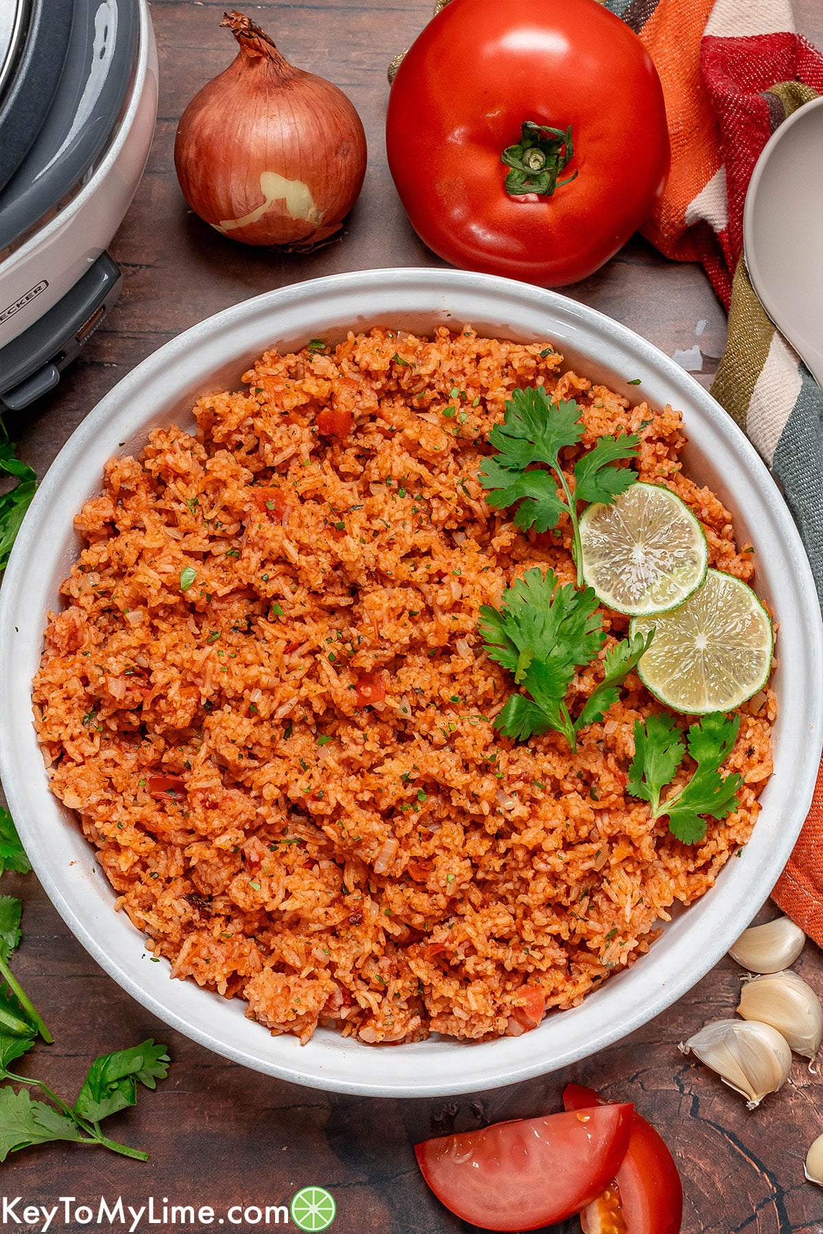 An overhead image of a serving dish filled with Mexican rice and garnish to the side.