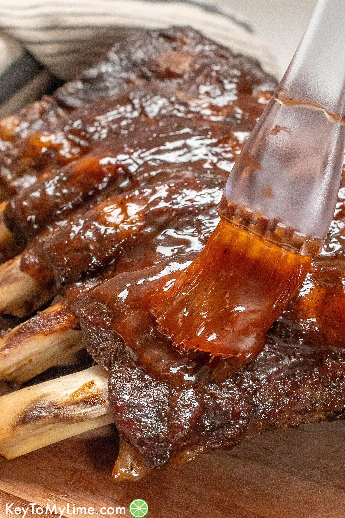 Basting BBQ sauce on beef ribs after broiling.