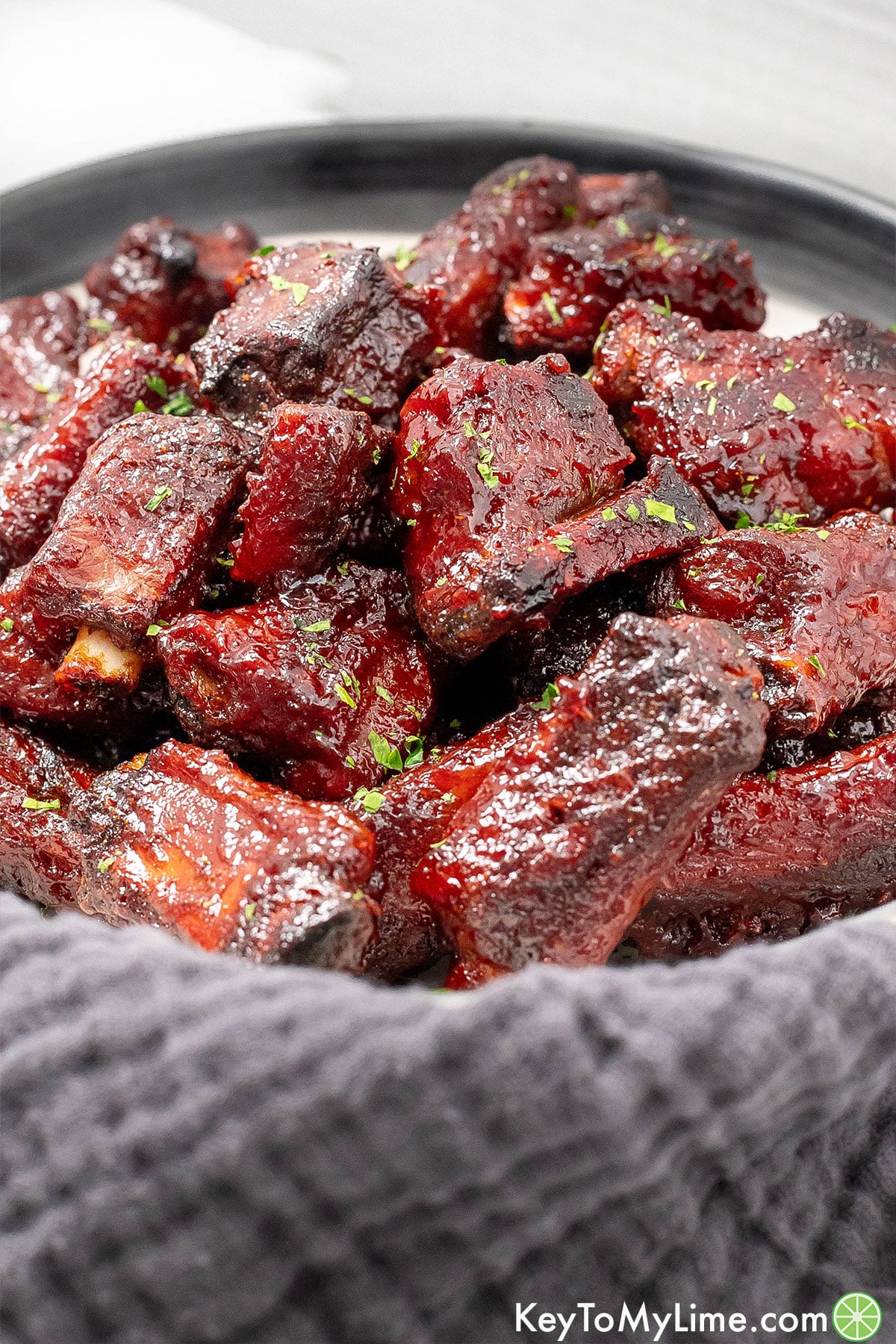 A side image of a bowl filled with baked riblets next to a napkin.