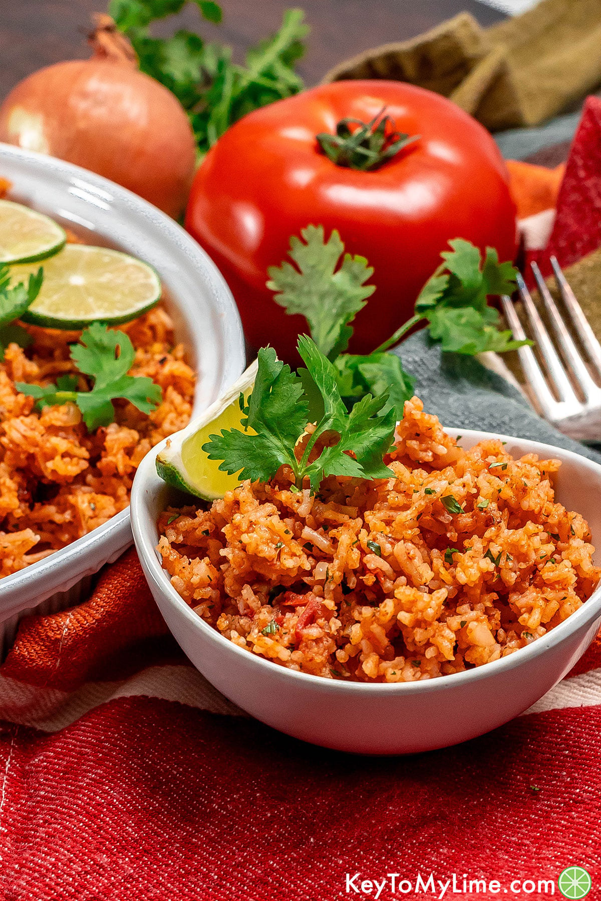 A side image of a serving of Mexican rice in a small bowl with fresh lime and cilantro.