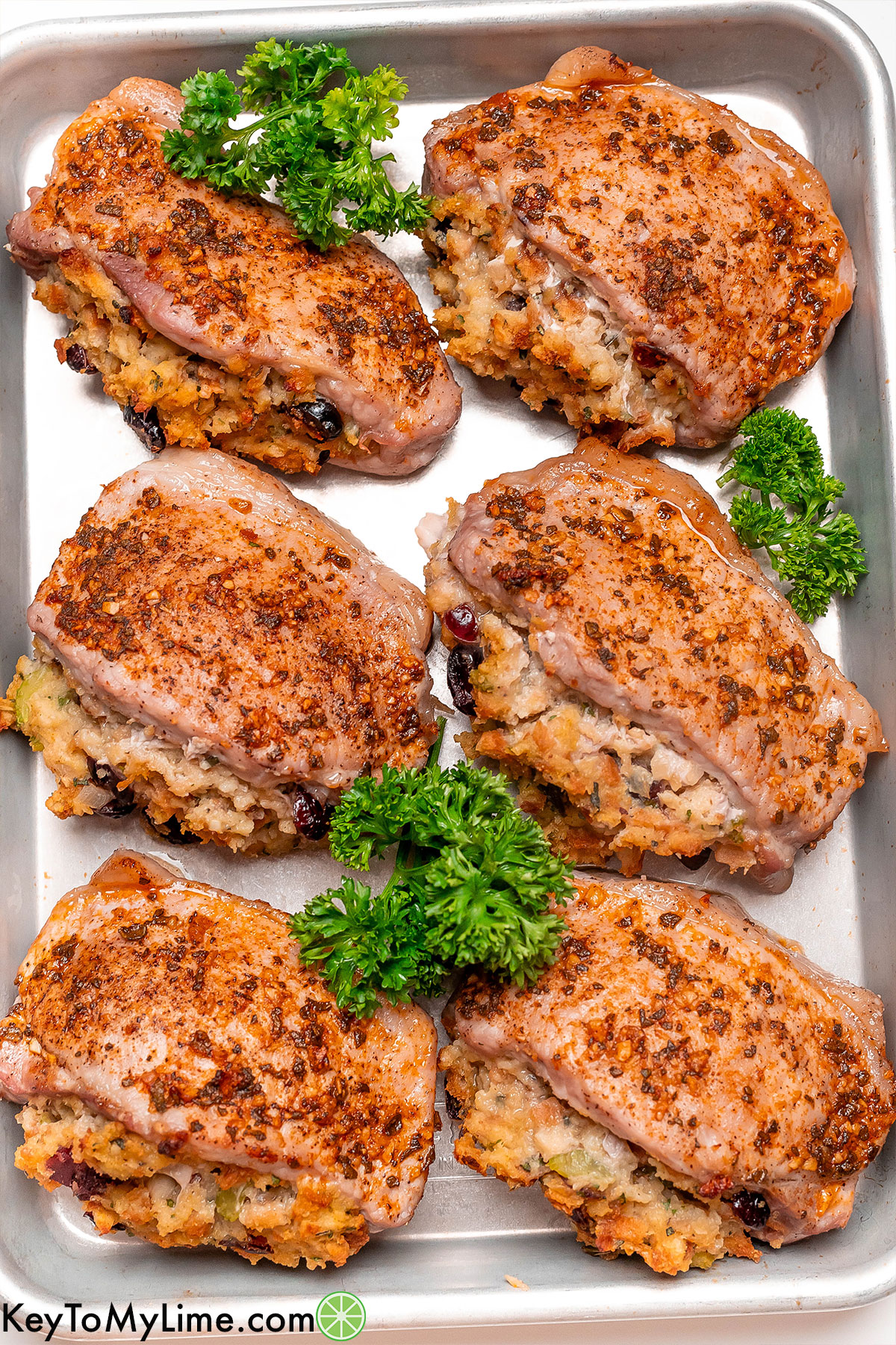 Six stuffed pork chops on a baking tray with parsley garnish.