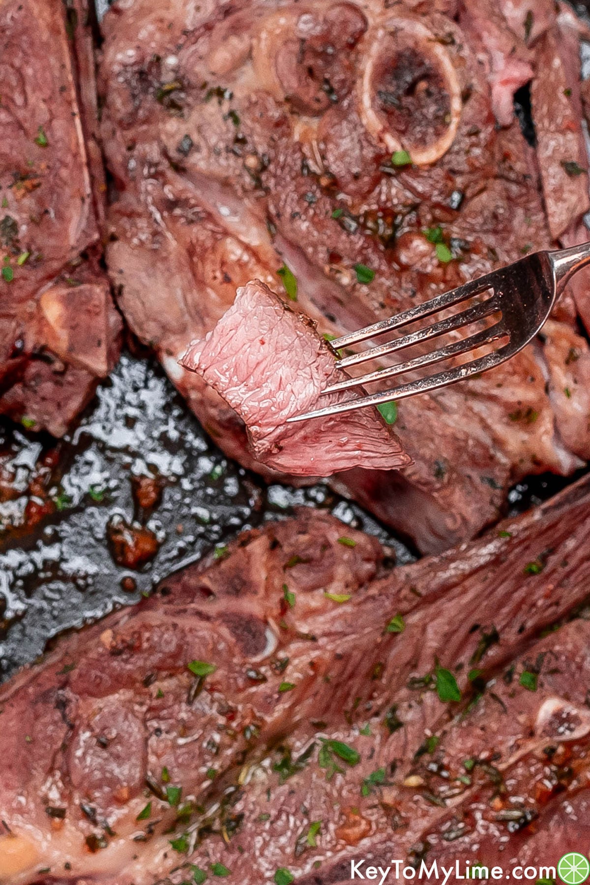A close up overhead image of a sliced lamb chop on a fork.