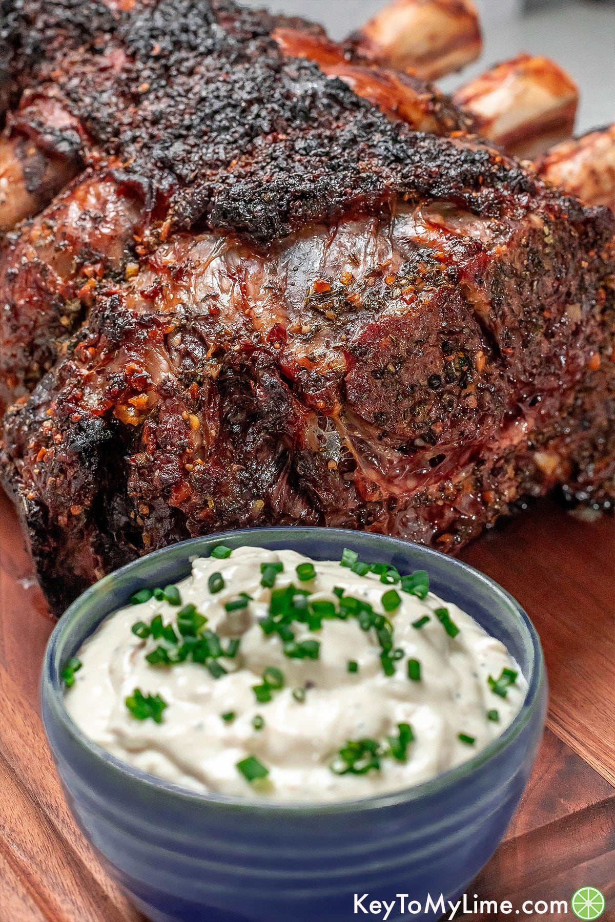 A ribeye roast resting on a cutting board next to a small bowl of horseradish sauce.